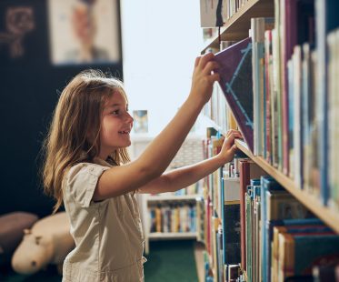 Schoolgirl choosing book in school library. Smart girl selecting literature for reading. Books on shelves in bookstore. Learning from books. School education. Benefits of everyday reading. Child curiosity. Back to school